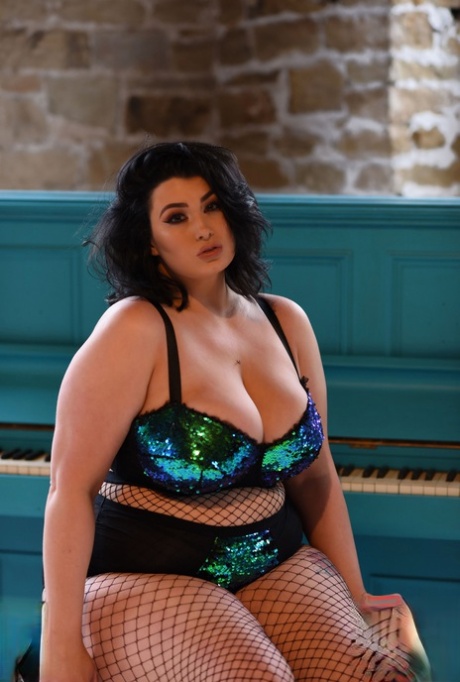 BBW babe Kiki poses in fishnets & strips to cradle her colossal breasts