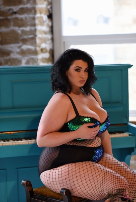 BBW babe Kiki poses in fishnets & strips to cradle her colossal breasts