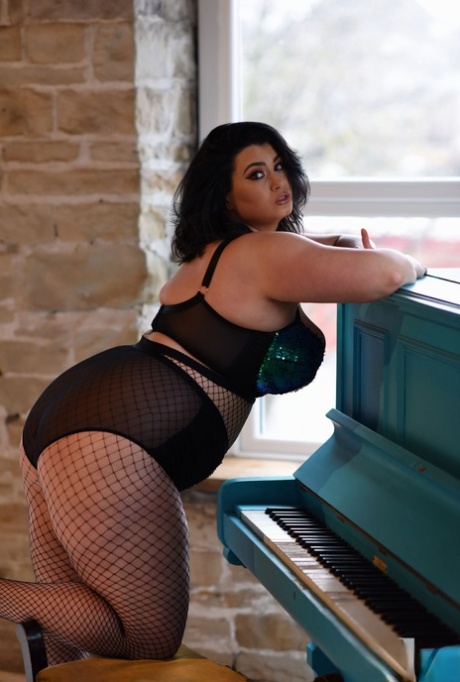 BBW babe Kiki poses in fishnets & strips to cradle her colossal breasts