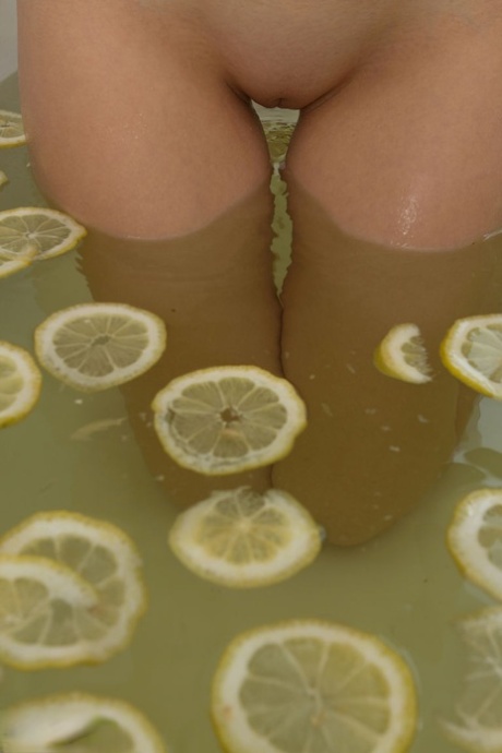Cute blonde young adult sinks her bald twat into a tub filled with lemon slices