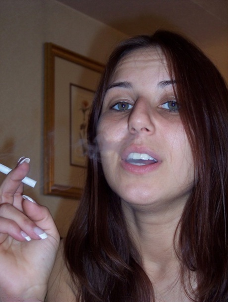 Totally natural girl Lexxxi sits on her bed while smoking a cigarette